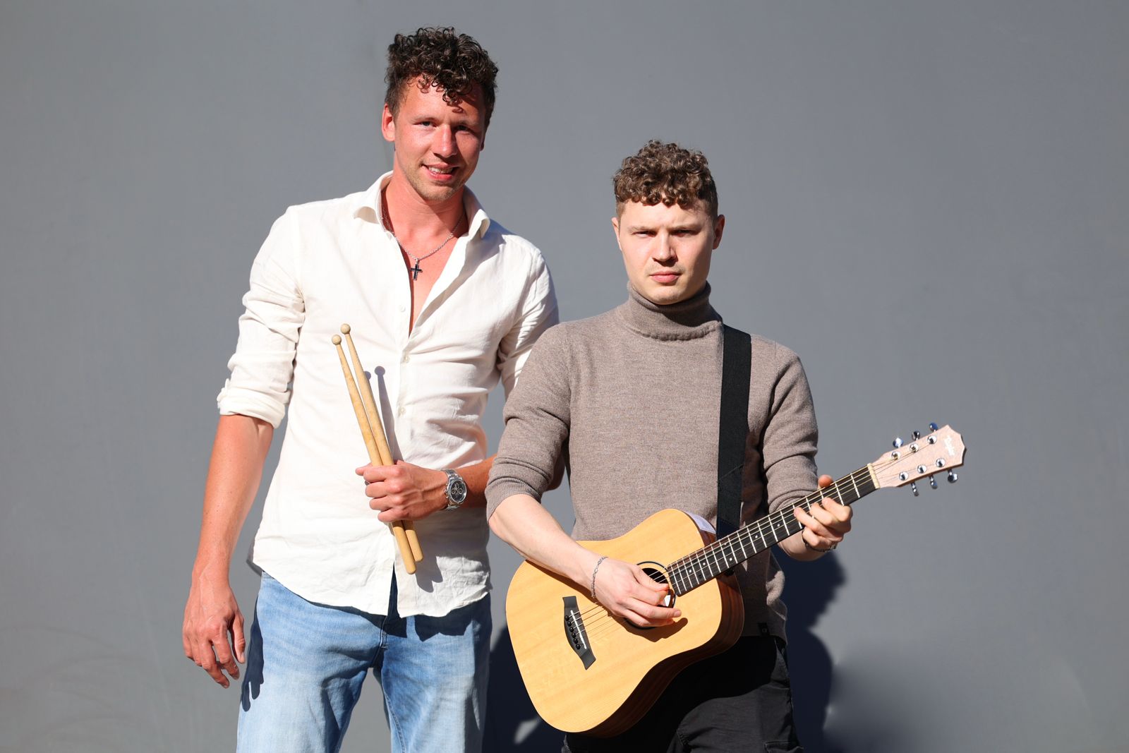 Zwei Männer stehen mit Instrumenten vor grauem Hintergrund, bereit für einen Auftritt als Julien-und-Xandi-Duo.