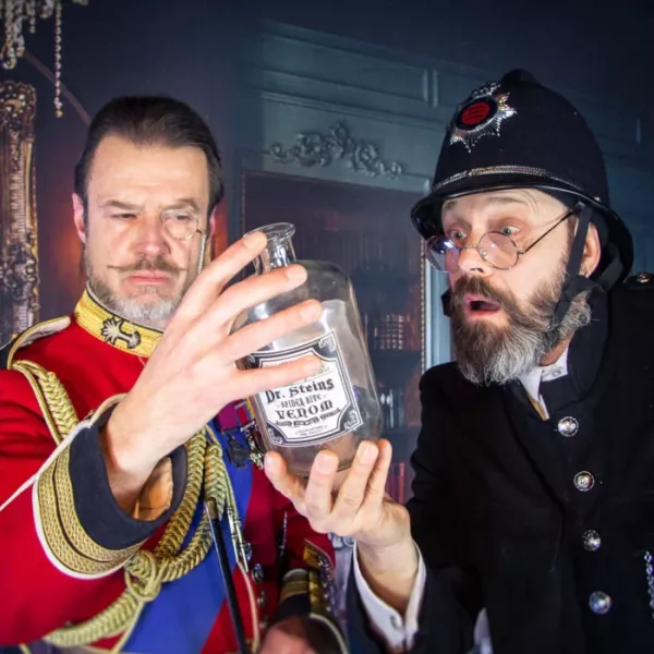 Zwei Männer in historischer Kleidung betrachten neugierig eine Flasche mit der Aufschrift „Dr. Steins Venom“ in einem geheimnisvollen Raum.