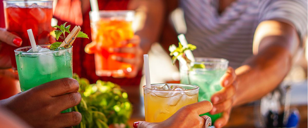 Eine fröhliche Gruppe stößt mit bunten Cocktails in einem Strandcafé an, um den nordischen Sommer zu feiern.