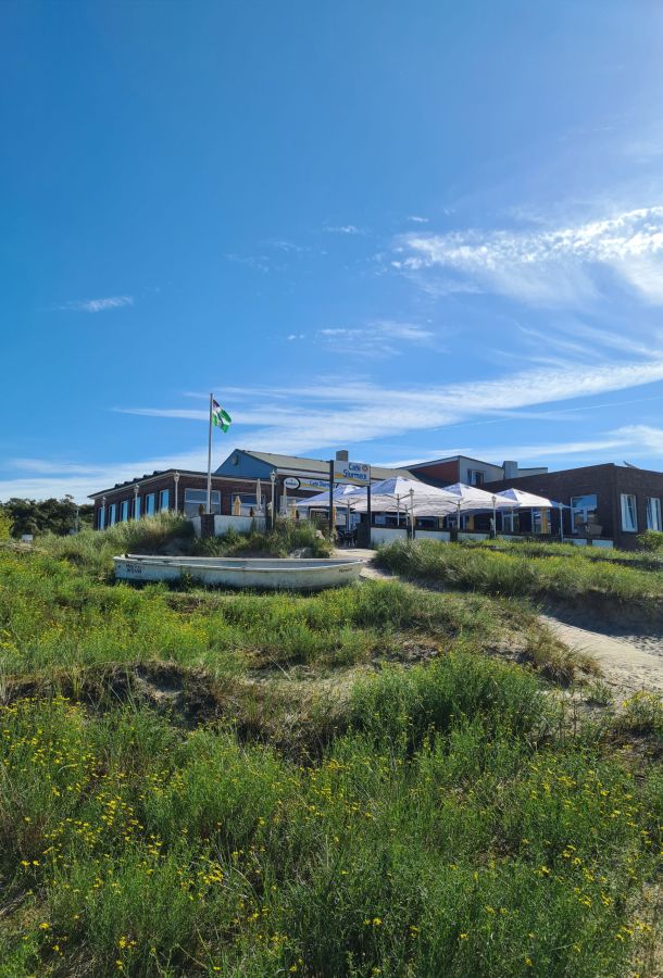 Das Strandcafé Sturmeck auf Borkum liegt idyllisch zwischen Dünen und blühenden Wiesen unter einem strahlend blauen Himmel.