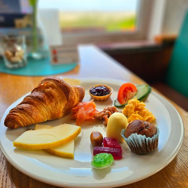 Ein reichhaltiges Frühstück mit Croissant, Käse, Lachs und mehr wird im Strandcafé Sturmeck serviert.