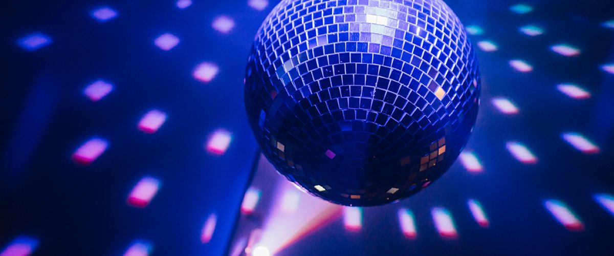 Eine glitzernde Discokugel wirft bunte Lichtreflexe im dunklen Raum und sorgt für eine lebhafte Atmosphäre.