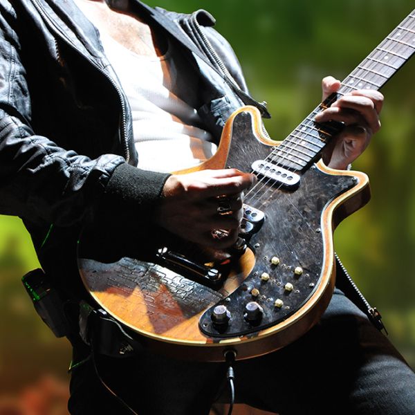 Ein Gitarrist spielt leidenschaftlich auf einer E-Gitarre, umgeben von buntem Bühnenlicht.