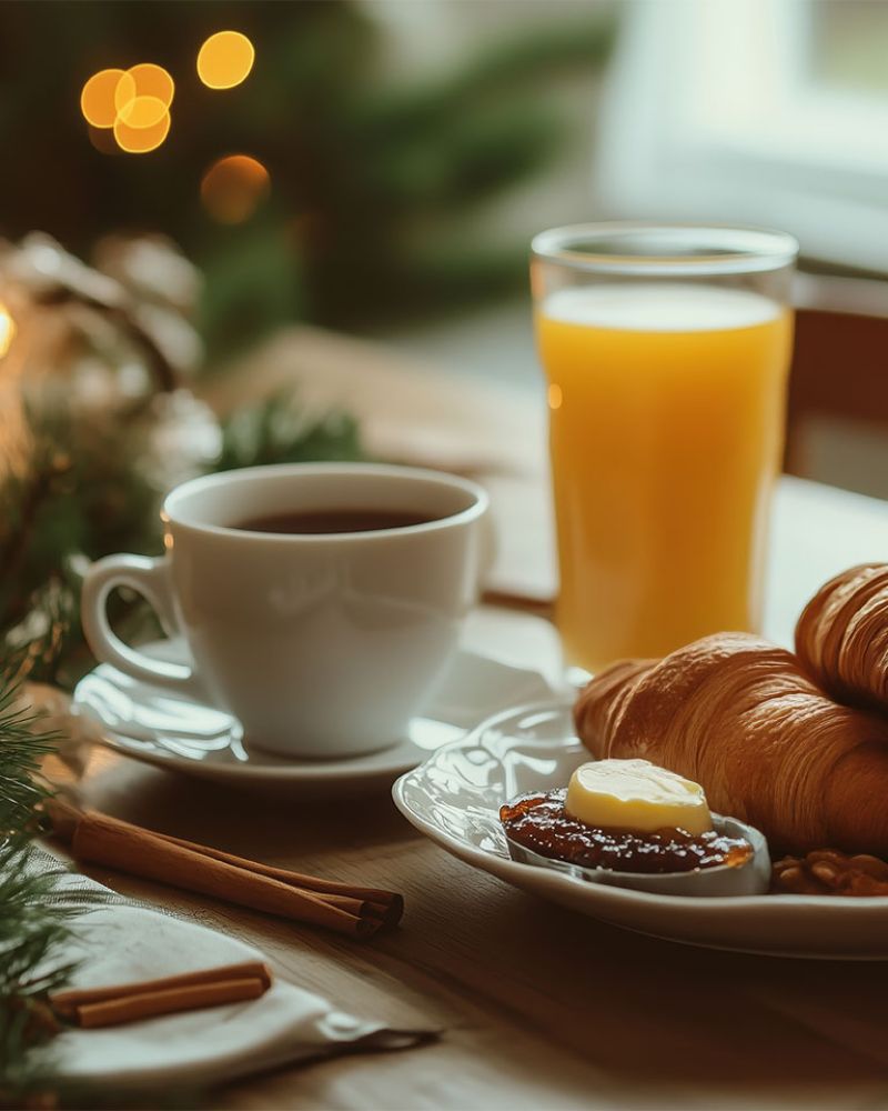 Gemütliches Frühstück mit Croissants, Kaffee und Orangensaft auf einem stimmungsvoll dekorierten Tisch bei Kerzenschein.