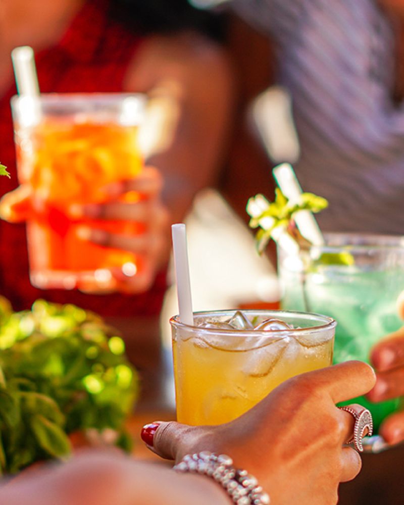 Eine fröhliche Gruppe stößt mit bunten Cocktails in einem Strandcafé an, um den nordischen Sommer zu feiern.