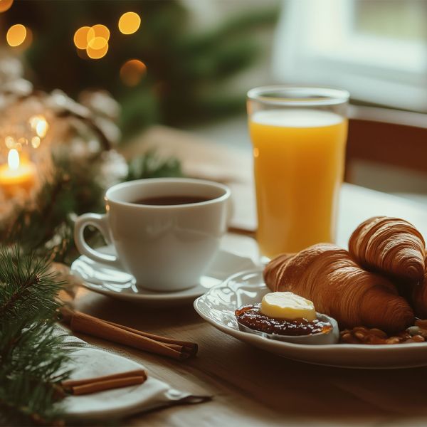 Gemütliches Frühstück mit Croissants, Kaffee und Orangensaft auf einem stimmungsvoll dekorierten Tisch bei Kerzenschein.