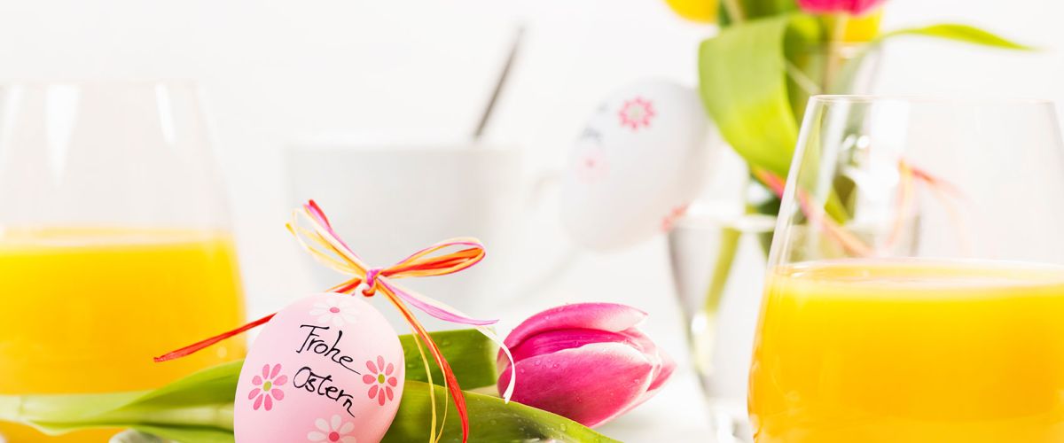 Ein festlich gedeckter Ostertisch mit bemaltem Ei, Tulpe und Orangensaft verbreitet fröhliche Frühlingsstimmung.