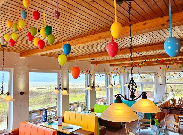 Bunt dekoriertes Strandcafé mit farbenfrohen Ostereiern an der Decke und gemütlichen Sitzplätzen mit Meerblick.